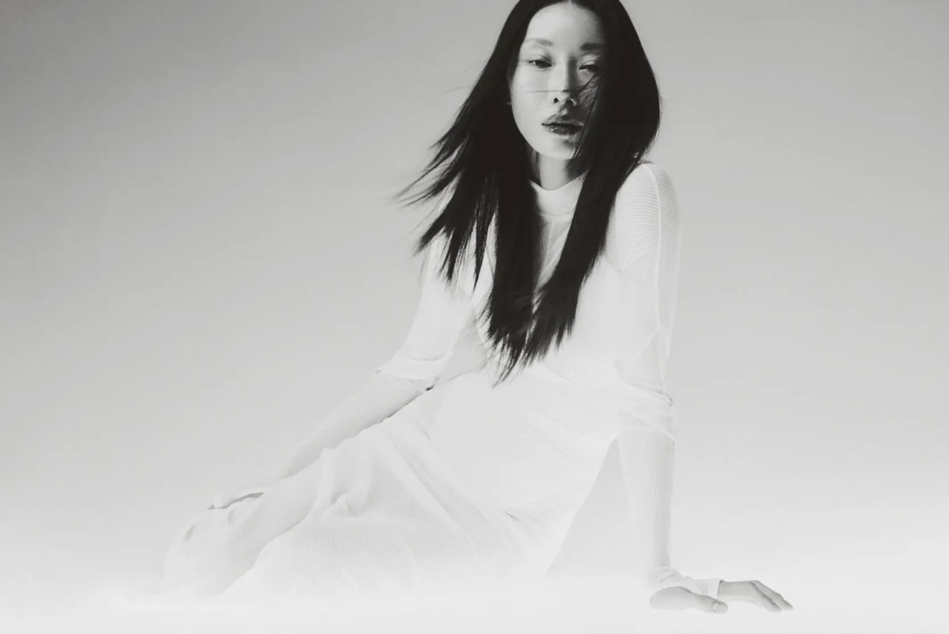 MIOGI LI — seated figure in a white ribbed dress, black-and-white