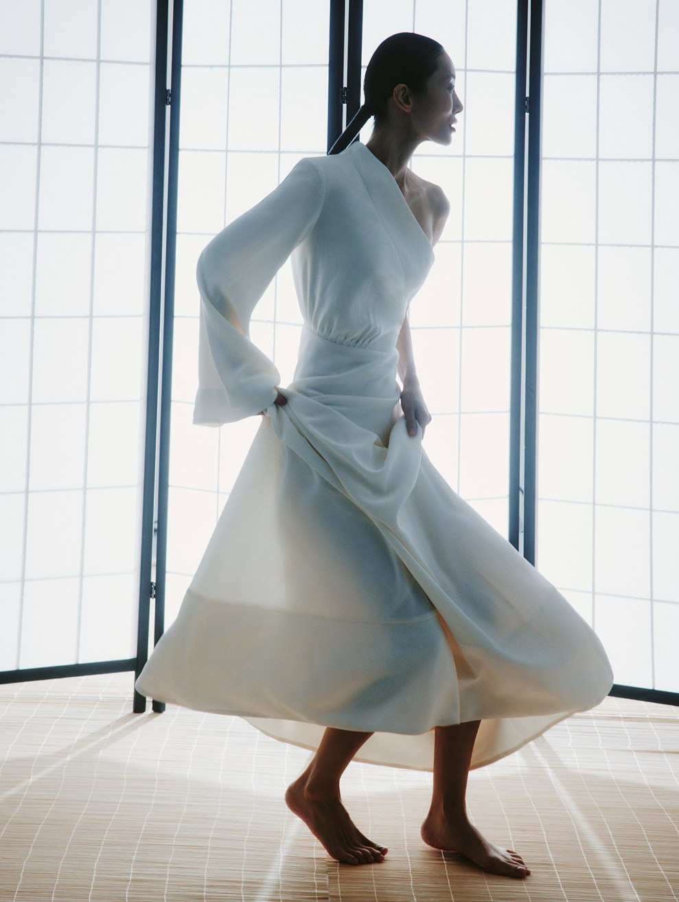 MIOGI LI — white one-shoulder dress in motion at a shoji screen