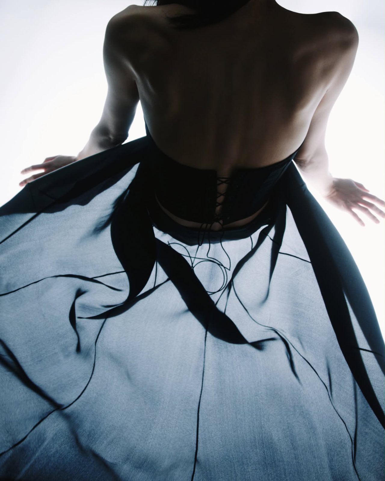 Editorial — bare back in a laced corset with black chiffon against the light