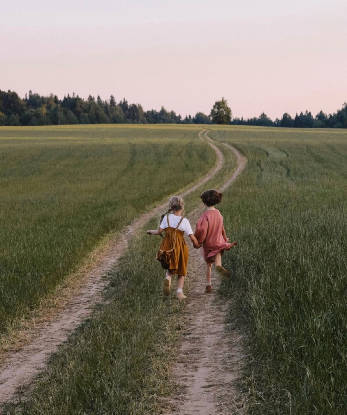 POLUSHA — campaign, two girls running hand in hand along a field path at dusk